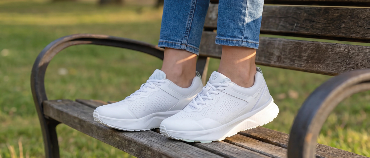 Dame sitzt auf Parkbank und trägt weiße Joya Sneaker.