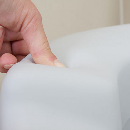Person drückt mit Daumen auf Toilettensitzerhöhung um zu demonstrieren das der Sitz weich ist. 