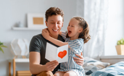 Vater und Tochter betrachten lächelnd eine selbstgemalte Karte zum Vatertag.