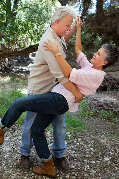 Mittelaltes Paar tanzt gemeinsam im Grünen, umgeben von Natur und Bäumen.