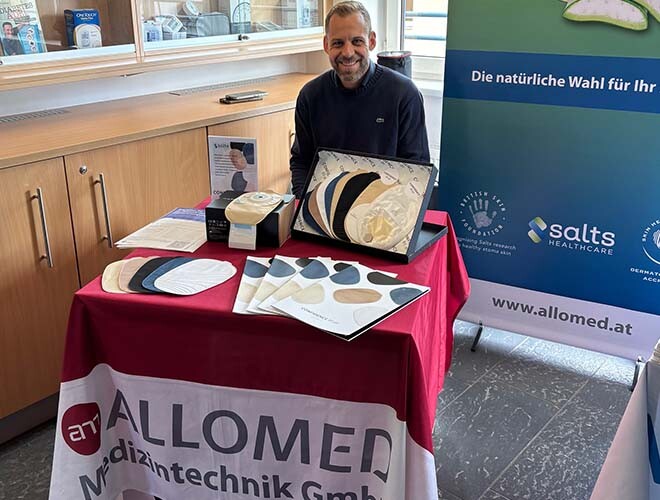 Ein Mitarbeiter von ALLOMED Medizintechnik GmbH sitzt am Infotisch mit Stomaprodukten beim Stoma-Infotag.