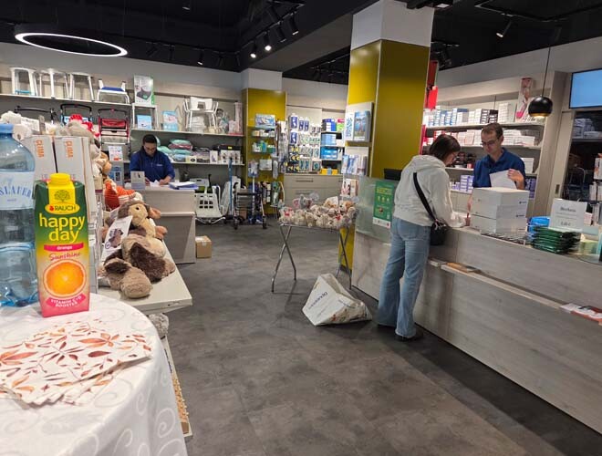 Freundliche Atmosphäre in der neu eröffneten bständig Filiale in Döbling mit Mitarbeiterin an der Kassa, Kundin und teilweise sichtbarem Tisch mit Snacks.