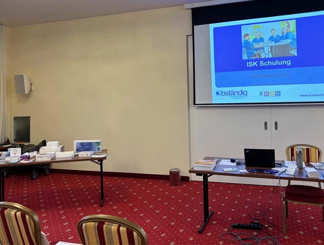 Seminarraum beim bständig ISK-Seminar vor Beginn: Vortragstisch mit Präsentation, Produkte auf Nebentisch, vorbereiteter Raum.