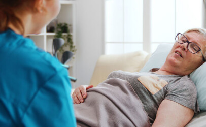 Eine Frau liegt im Bett und spricht mit medizinischer Mitarbeiterin.