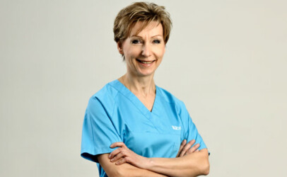 Freundlich lächelnde bständig Krankenschwester in blauer Dienstkleidung vor hellem Hintergrund.