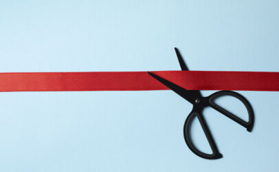 Schere schneidet rotes Band vor blauem Hintergrund als Symbol für die Neueröffnung.