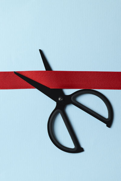 Schere schneidet rotes Band vor blauem Hintergrund als Symbol für die Neueröffnung.