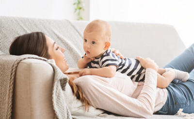 Mutter liegt mit ihrem Baby auf Sofa.