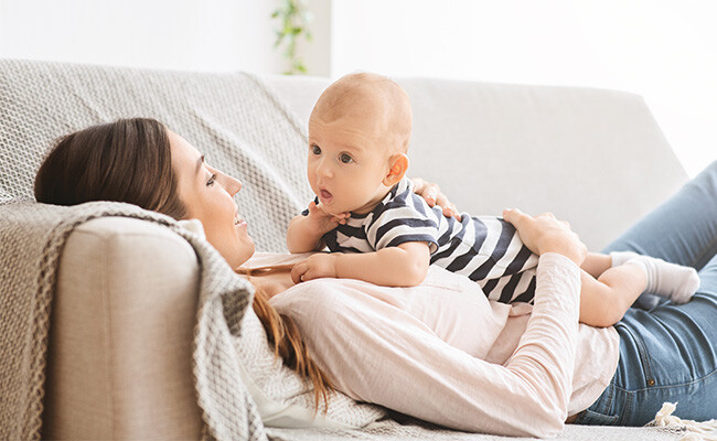 Mutter liegt mit ihrem Baby auf Sofa.