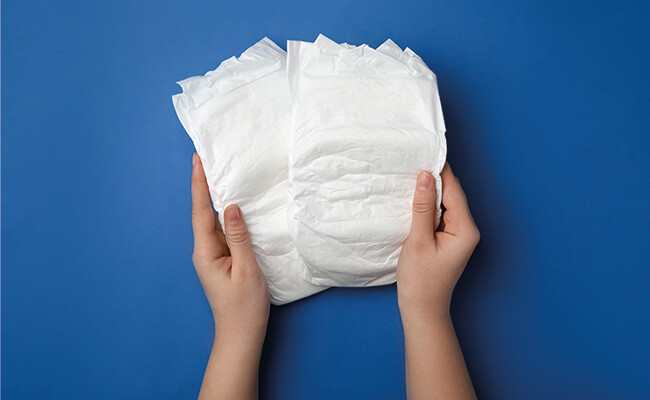 Zwei Hände halten Windeln vor einem blauen Hintergrund.