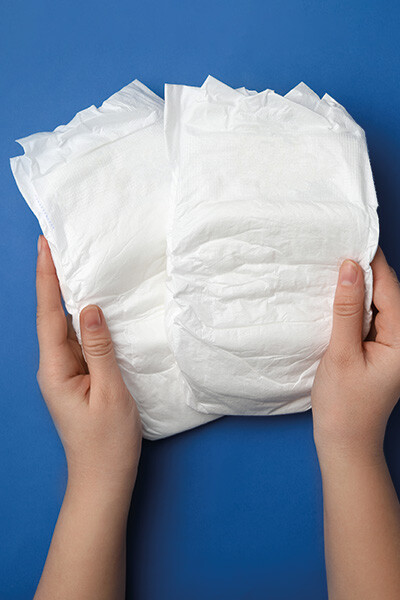 Zwei Hände halten Windeln vor einem blauen Hintergrund.