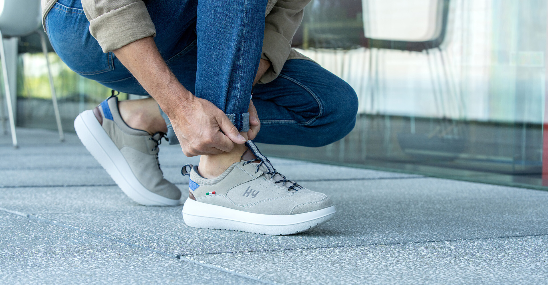 Person kniet im Freien und zieht einen grauen Sneaker mit weißer Sohle an.