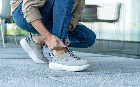 Person kniet im Freien und zieht einen grauen Sneaker mit weißer Sohle an.