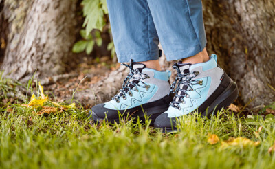 Person steht auf einer Wiese und trägt hellblaue Outdoor-Schuhe mit schwarzer Sohle.