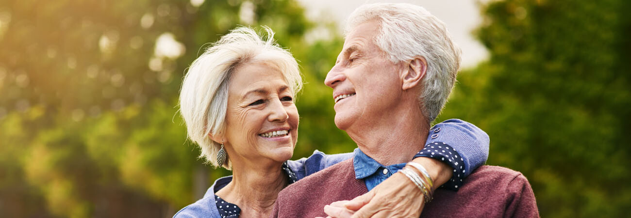 Paar umarmt sich lächelnd in der Natur, Blickkontakt, verschwommener Hintergrund.