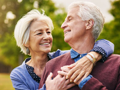 Paar umarmt sich lächelnd in der Natur, Blickkontakt, verschwommener Hintergrund.