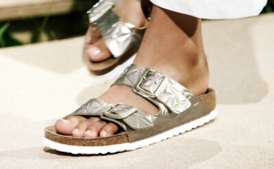 Füße einer Frau in Birkenstock-Sandalen, ein Fuß im Vordergrund, weiße Hose teilweise sichtbar
