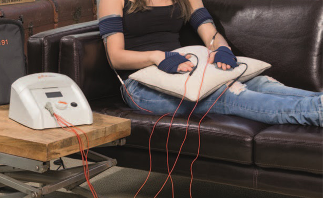 Frau sitzt auf Sofa und hat Elektroden an Ihren Händen.