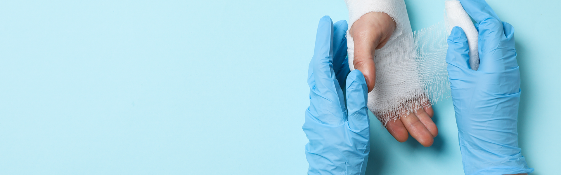 Zwei Hände die Handschuhe tragen versorgen eine andere Hand mit einem Verband auf blauem Hintergrund.