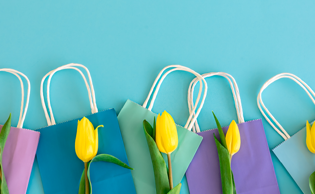 Collage auf hell blauem Hintergrund mit bunten Einkaufstüten und gelben Tulpen.