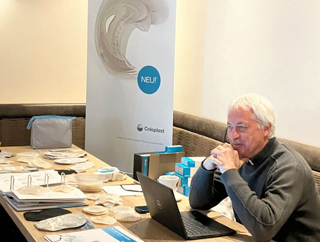 Firmenvertreter sitzt am Ausstellungstisch mit Stoma-Materialien beim bständig Stoma-Seminar Krems 2026.