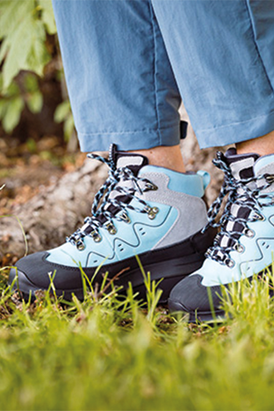 Person steht auf einer Wiese und trägt hellblaue Outdoor-Schuhe mit schwarzer Sohle.