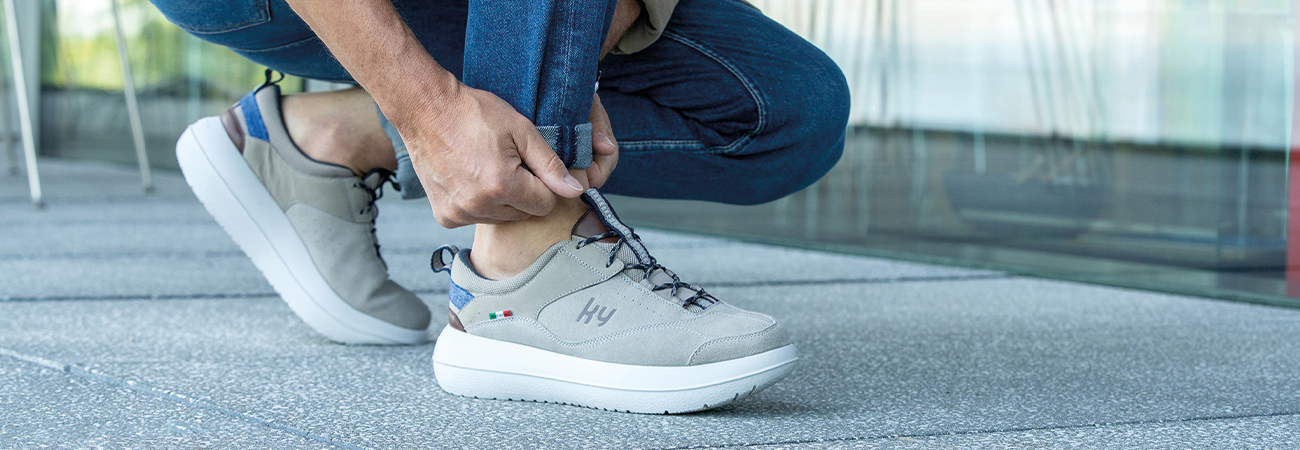 Person kniet im Freien und zieht einen grauen Sneaker mit weißer Sohle an.