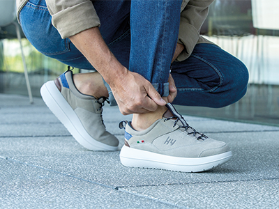 Person kniet im Freien und zieht einen grauen Sneaker mit weißer Sohle an.