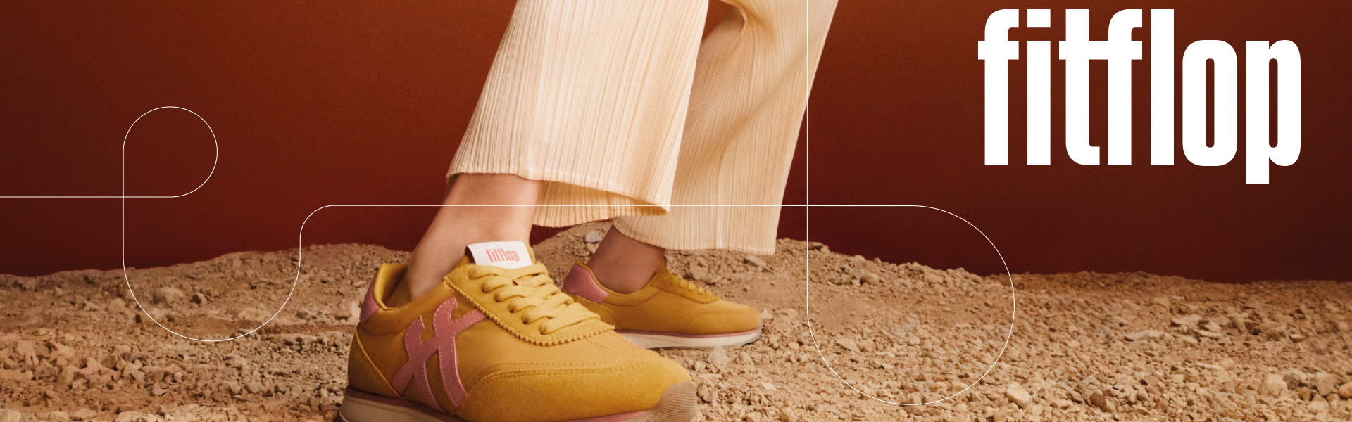 Fitflop Banner, Person trägt Hellbraune fitflop Schuhe und steht auf Schotter, der Hintergrund ist braun.