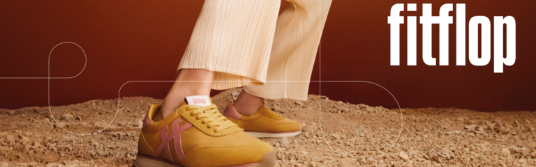 Fitflop Banner, Person trägt Hellbraune fitflop Schuhe und steht auf Schotter, der Hintergrund ist braun.